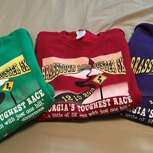 Stack of Gildan Brasstown Bald Buster 5K Kids Sweatshirts - Red, Green, Purple